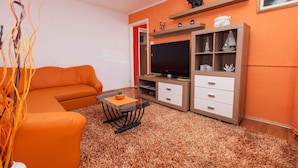 A living room with an orange sofa, a TV on a wooden stand, and a small table with a vase.