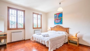 A bedroom with a large bed, two windows, a radiator, a desk, and a painting on the wall. - Cozy apartment in S.Martino in Colle LU with swimming pool (S.Martino in Colle LU)