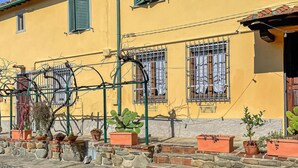 A yellow building with green shutters, potted plants, and a metal structure with wires. - Cozy apartment in S.Martino in Colle LU with swimming pool (S.Martino in Colle LU)