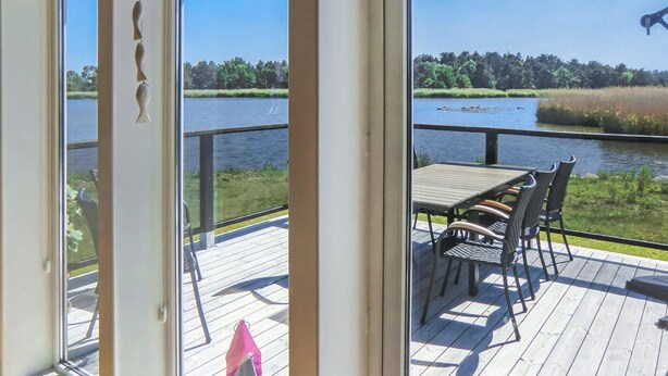 A deck with a table and chairs overlooking a lake with a forested shoreline. - 2 bedroom lovely home in Kalmar (Kalmar)