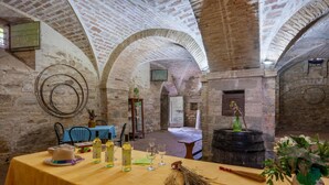 Un intérieur aux murs de pierre, aux plafonds en arc de cercle, une table dressée avec des bouteilles et des verres, et un balai.