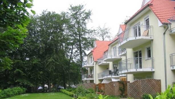 A multi-story building with balconies, surrounded by a well-maintained garden and trees. - * FeWo Hansel GM 69372 - FeWo Hansel (Graal-Müritz)