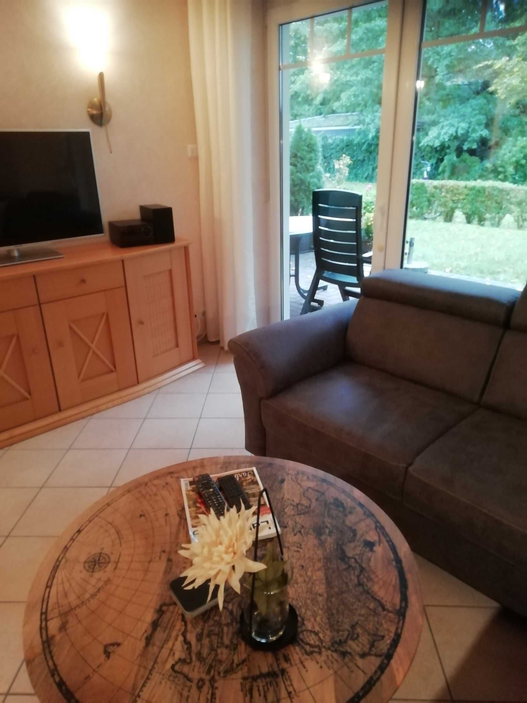 Ein Wohnzimmer mit Fernseher auf einer Holzkommode, einem braunen Sofa und einem Couchtisch mit einem dekorativen Gegenstand.
