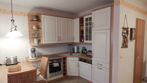 A compact kitchen with white cabinets, a built-in oven, a sink, and a dining area with wicker chairs. - * FeWo Hansel GM 69372 - FeWo Hansel (Graal-Müritz)