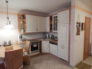 Una cucina compatta con mobili bianchi, forno integrato, lavandino e zona pranzo con sedie in vimini.