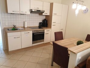 Una cocina moderna con armarios blancos, un horno de acero inoxidable y una mesa de comedor de madera con sillas.
