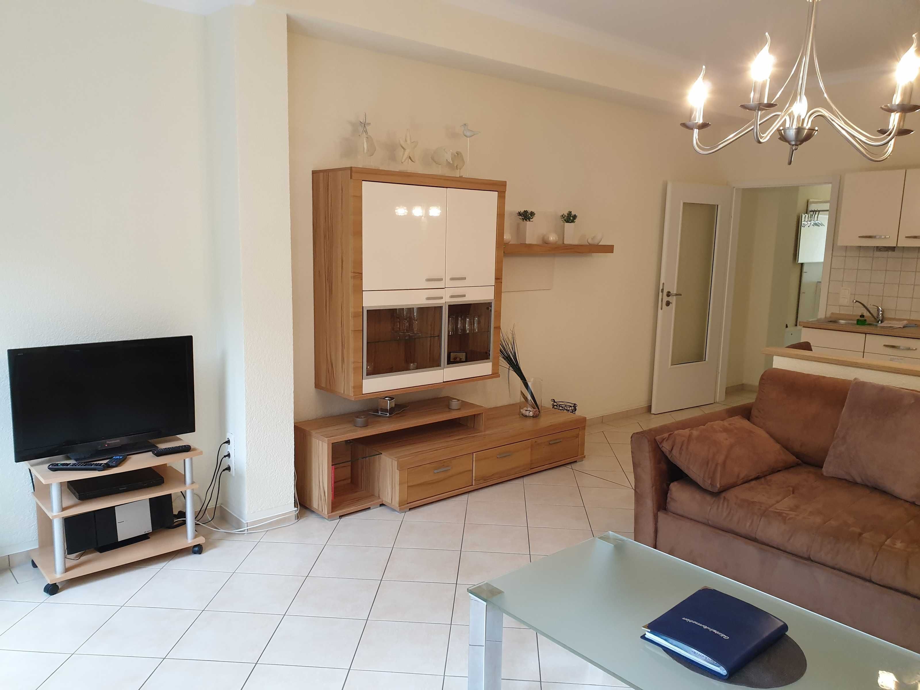 Un salon avec un téléviseur, un meuble de rangement en bois, une table basse en verre et un canapé marron.