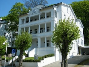 A white building with a central entrance, multiple windows, and a sign with a 'Q' logo.
