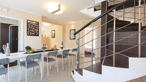 Un intérieur moderne agrémenté d’un escalier en colimaçon, d’un coin repas avec une table et des chaises, et d’œuvres d’art accrochées aux murs.