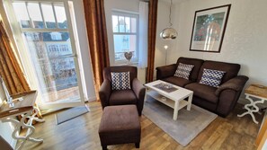 Ein Wohnzimmer mit einer Sofagarnitur, einem Couchtisch, einem Beistelltisch und einem Fenster mit Vorhängen.