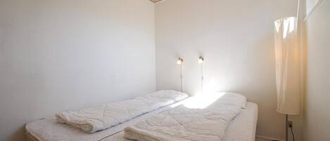 Een kleine, schone kamer met twee bedden, een houten plafond en een bedlampje.
