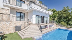Ett modernt hus i två våningar med en swimmingpool, en fasad av sten och flera balkonger.