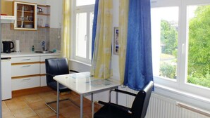 A small kitchen with a table and chairs, a window with curtains, and a view of greenery outside.