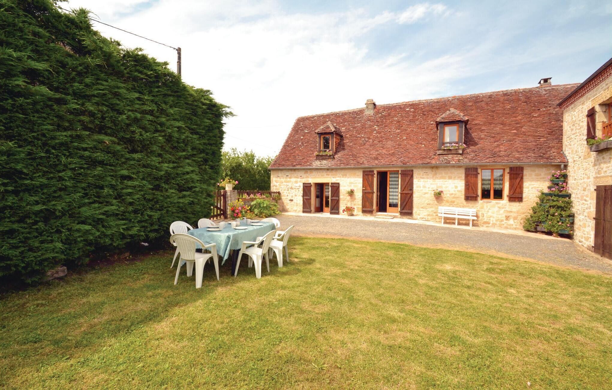 A stone house with a red-tiled roof, a grassy yard, and a table set for dining.