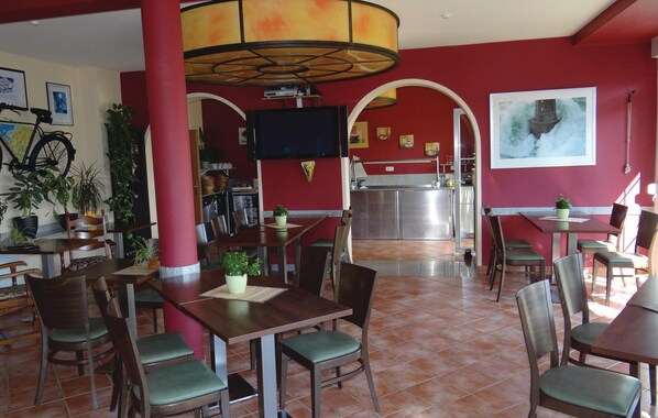 A restaurant with red walls, a tiled floor, and a television mounted on the wall. There are multiple tables and chairs, and a large window in the background. - Beautiful home in Insel Poel/Kirchdorf (Insel Poel/Kirchdorf)