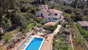 Uma casa de dois andares com piscina, cercada por árvores e colinas.