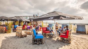 Angolo relax in spiaggia con pallet di legno e cuscini colorati, riparato da ampie ombrelloni e vista sul mare.
