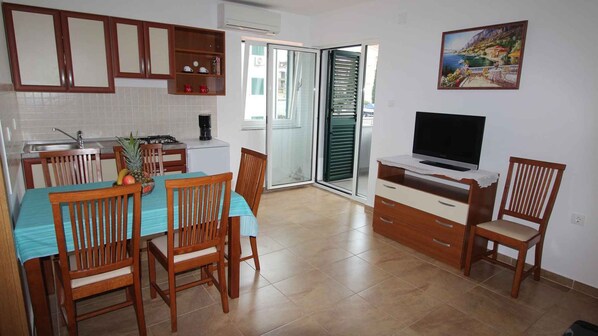 A kitchen with a dining table, chairs, a TV, and a sliding glass door leading to a balcony.