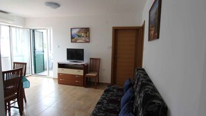 A living room with a sofa, a TV on a wooden cabinet, a chair, and a door. - Holiday apartment with balcony (Malinska)