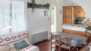 Ein gemütliches Zimmer mit einer Couch, einem Esstisch mit Stühlen, Holzschränken und einem Fenster mit durchsichtigen Vorhängen.