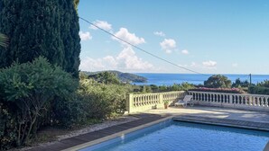 Ein Schwimmbecken mit Meerblick, umgeben von Grün und einer Holzterrasse.
