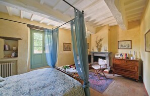 Ein Schlafzimmer mit einem Himmelbett, einem Kamin, einer hölzernen Kommode und einer Heizung.