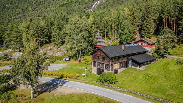 A wooden cabin with a stone foundation, surrounded by dense forest and a mountain backdrop. - Stunning home in Dølemo with sauna (Dølemo)