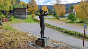 A statue of a person standing on a pedestal in a rural setting with a road, houses, and autumn trees in the background. - Stunning home in Dølemo with sauna (Dølemo)