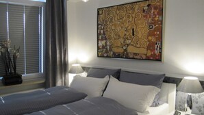 Et hotelværelse med en stor seng, to sengeborde, et natbord og et vindue med persienner.