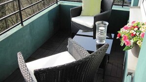 En balkon med fletmøbler, et glasstage og en blomsteropsætning.
