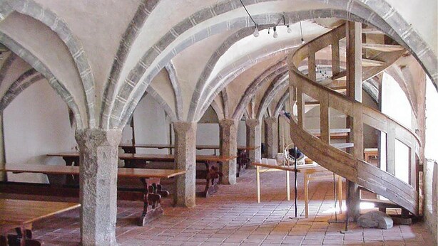 Rummelig indretning med hvælvede lofter og stensøjler, med en central spiraltrappe.