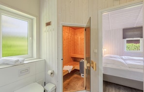 Ein Holzinnenraum mit Sauna, Bett und Fenster mit Blick auf Grünflächen.