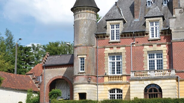 Ein historisches Gebäude mit einem markanten Turm, einem Rundbogenportal und zahlreichen Fenstern.