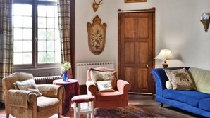 Ein traditionell eingerichteter Raum mit einer großen Holztür, einem blauen Sofa, zwei Sesseln, einem kleinen Tisch mit einer Vase und einem gemusterten Teppich.