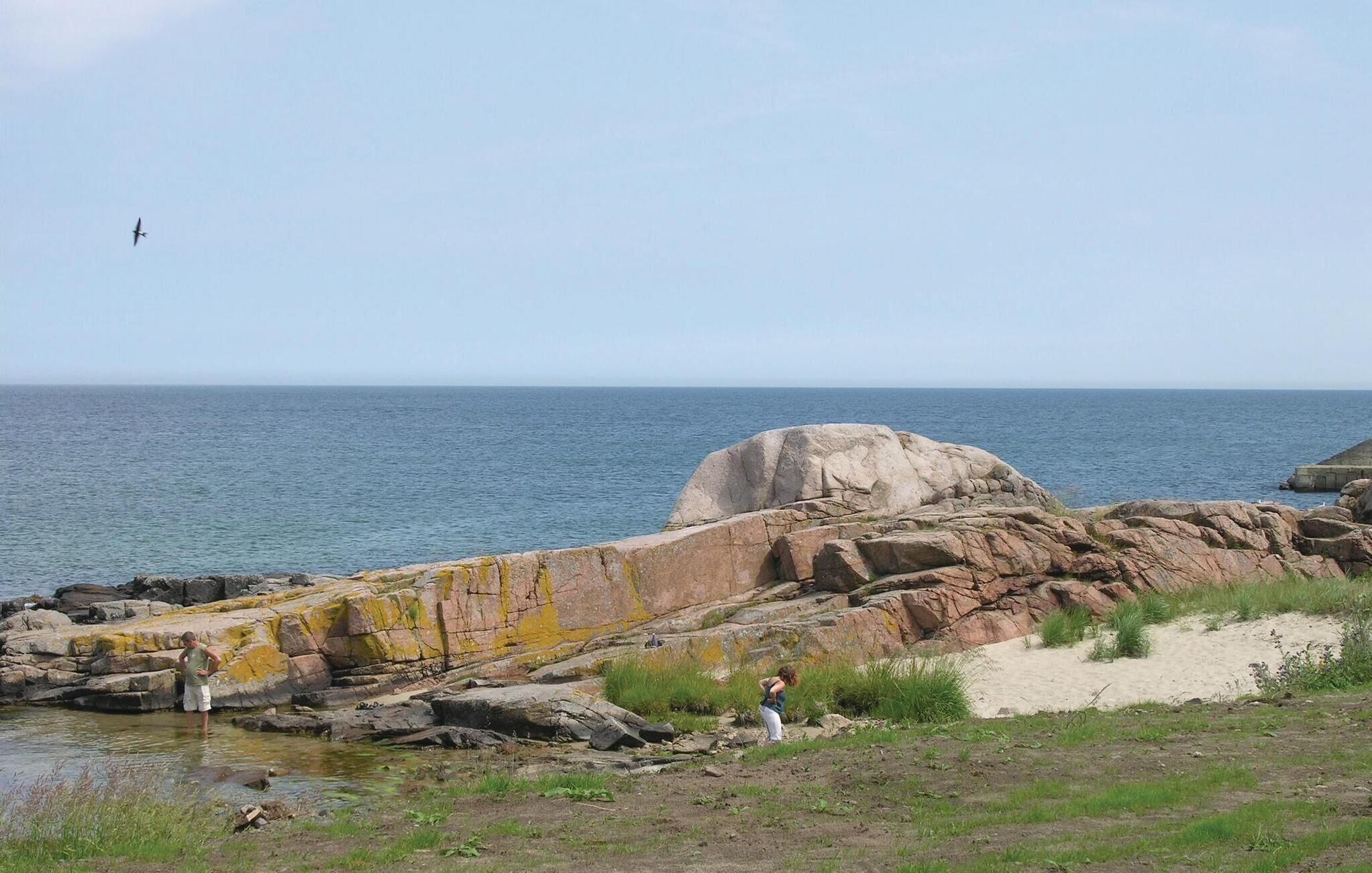 Paisatge costaner amb terreny rocos, un gran bloc de pedra i una vista clara del mar.