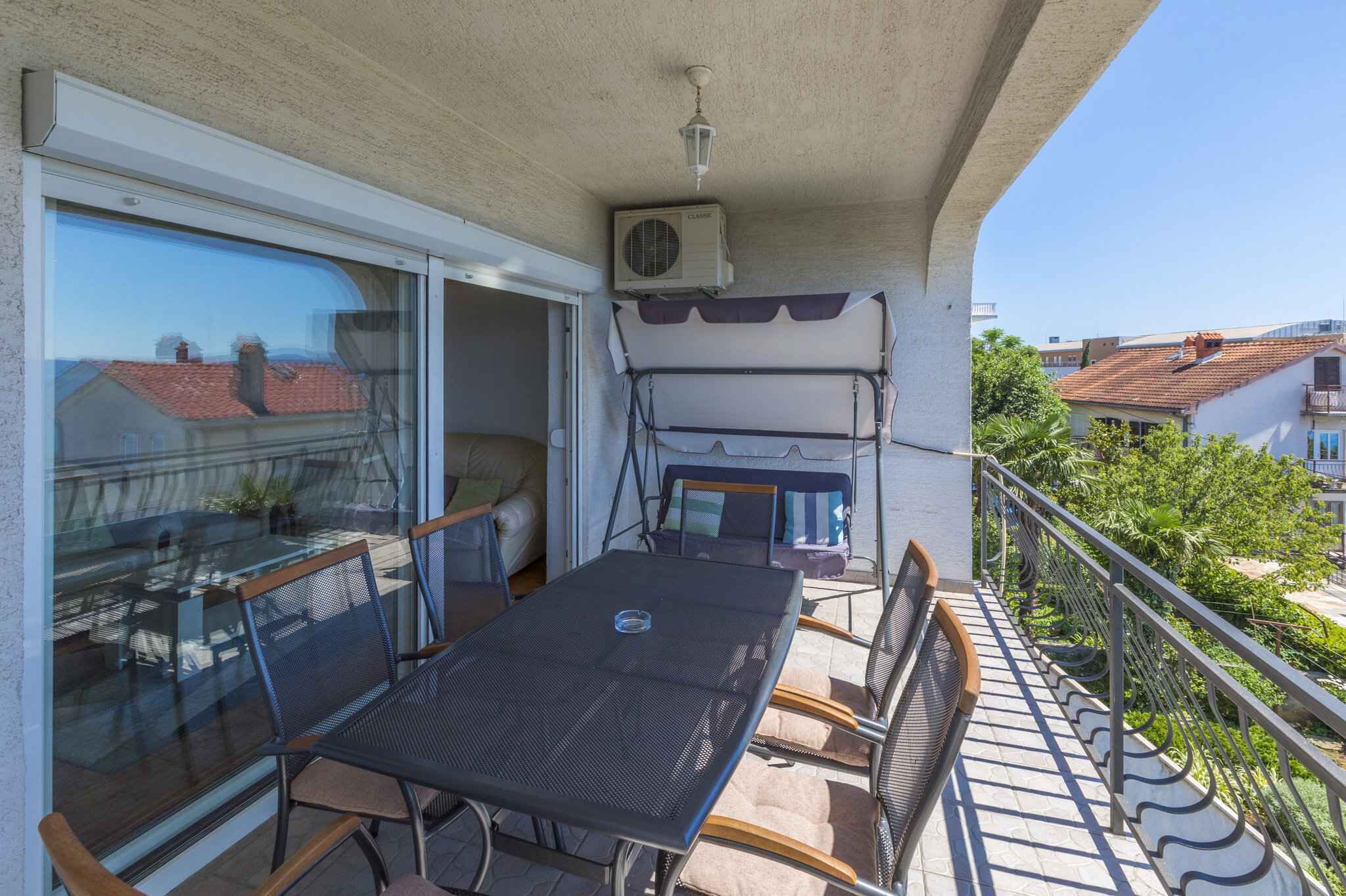 Un balcón con una mesa y sillas, un equipo de aire acondicionado y vistas al vecindario.