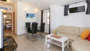 En moderne stue med en beige sofa, et spisebord med stole, et sofabord og et billede på væggen.