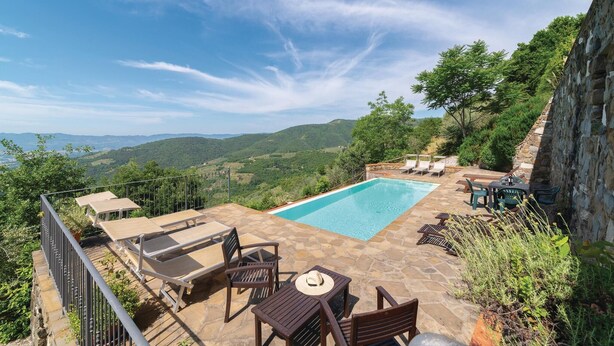 A pool area with lounge chairs and a table, surrounded by stone walls and greenery, overlooking a mountainous landscape. - Nice apartment in Loro Ciuffenna AR (Loro Ciuffenna AR)