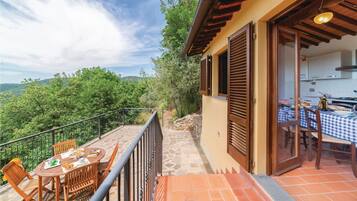 Un balcone con tavolo apparecchiato per mangiare, un angolo cottura con tavolo imbandito e vista sul verde circostante.