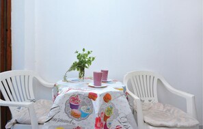 Ein kleiner Tisch mit einer Tischdecke mit Cupcake-Motiven, zwei weiße Plastikstühle und ein Blumentopf.