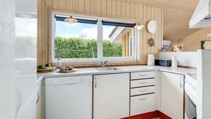 Cozinha com paredes de madeira, janela com vista para o verde, lava-louças Bosch e uma pia.