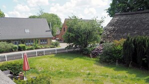 A backyard with a paved patio, a yellow table, and a red umbrella. - Apartment 1 - Horn: Vacation in a thatched house in Schleswig-Holstein (Silberstedt)