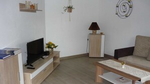 A modern living room with a flat-screen TV, a wooden coffee table, a sofa, a cabinet, and a lamp. - Apartment 1 - Horn: Vacation in a thatched house in Schleswig-Holstein (Silberstedt)