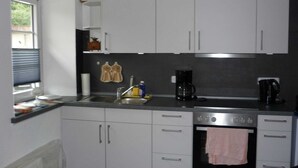 A kitchen with white cabinets, a stainless steel sink, a coffee maker, and an oven. - Apartment 1 - Horn: Vacation in a thatched house in Schleswig-Holstein (Silberstedt)