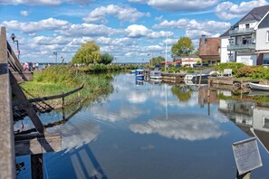 A calm river with boats, a wooden walkway, and buildings along the riverbank.