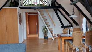 A loft-style room with exposed wooden beams, a wooden staircase, a dining area with wicker chairs, and a blue sofa. - Studio with bicycles in the Schaumburg district (Meerbeck)