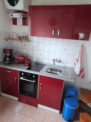 A compact kitchen with red cabinets, a built-in oven, a coffee maker, and a sink.