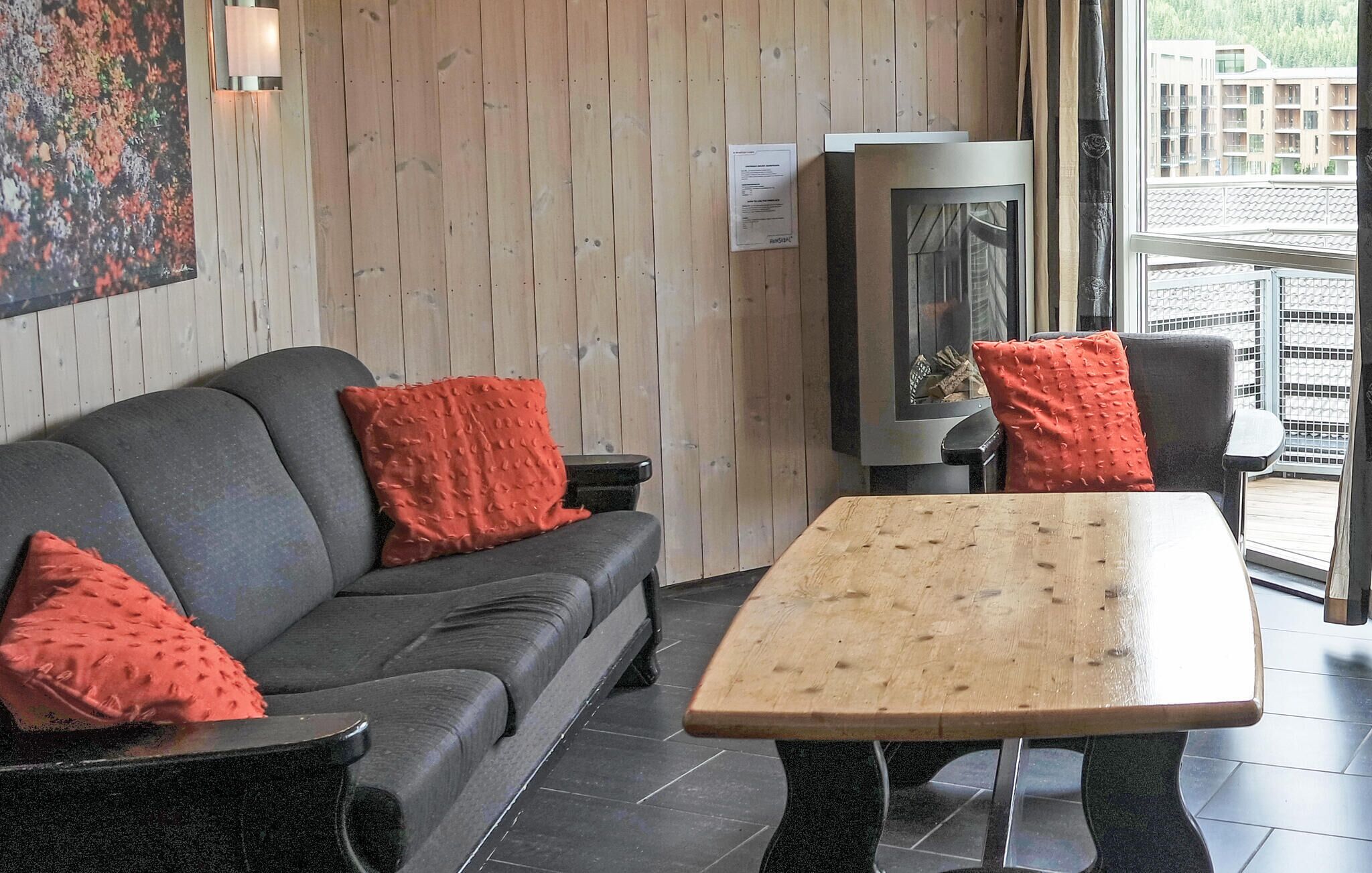 A modern interior with a grey sofa, red cushions, a wooden table, and a TV.