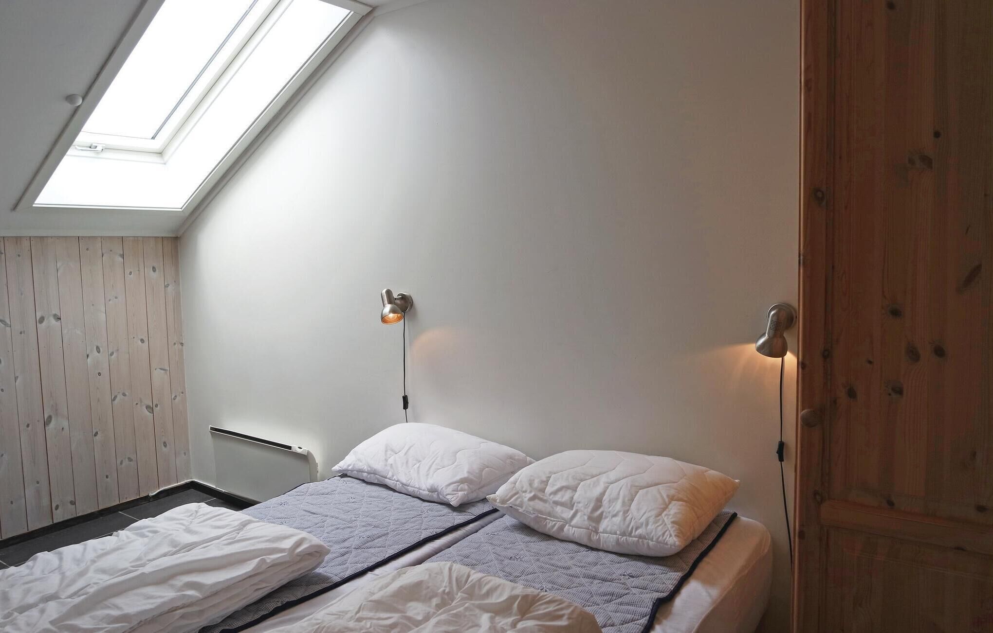 Un dormitorio con tragaluz, una cama con ropa de cama blanca y un armario de madera.