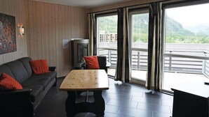 A modern living room with a wooden floor, a sofa with red cushions, a wooden coffee table, and a large window with a view of a balcony and mountains. - Pet friendly apartment in Hemsedal (Hemsedal)